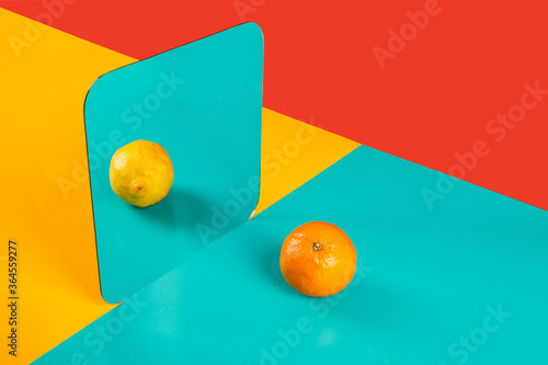 Vibrant background with mirror reflection of fresh orange as lemon on blue surface in composition with empty red and yellow areas like concept of perception in three dimensional space and distortion of imagination