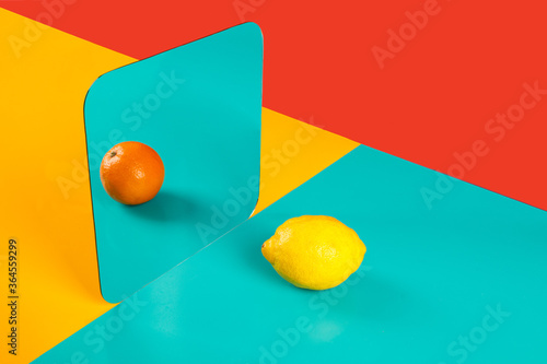 Vibrant background with mirror reflection of fresh orange as lemon on blue surface in composition with empty red and yellow areas like concept of perception in three dimensional space and distortion of imagination