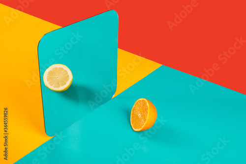 Vibrant background with mirror reflection of half of fresh orange as lemon on blue surface in composition with empty red and yellow areas like concept of perception in three dimensional space and distortion of imagination photo