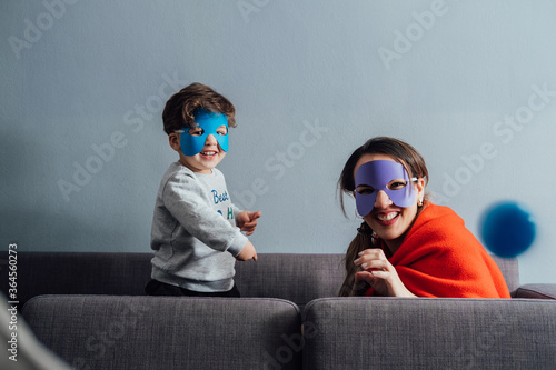 Cheerful woman and little boy wearing paper masks playing during weekend and pretending being superheroes while looking at camera photo