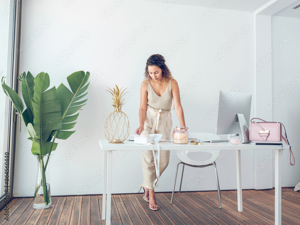 Beautiful female in elegant outfit reading notes in notepad while leaning on table in stylish office Beautiful female in elegant outfit reading notes in notepad while leaning on table in stylish office