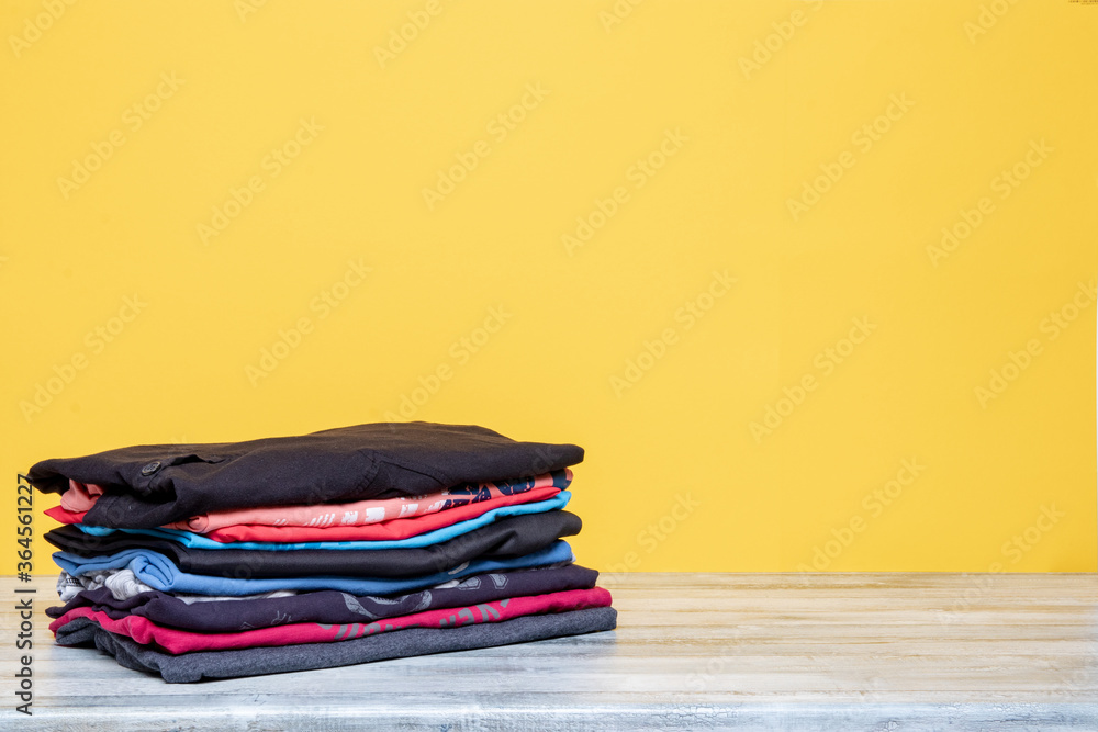 Pile of folded cotton t-shirts or shirts on a bright table with space for your display product montage on a yellow background. Summer fashion. Pile of folded cotton t-shirts or shirts on a bright table with space for your display product montage on a yellow background. Summer fashion.