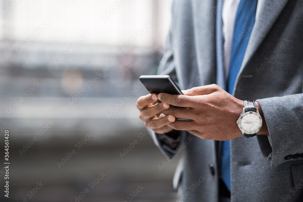 Faceless shot of black businessman in suit and watch using smartphone outside. Faceless shot of black businessman in suit and watch using smartphone outside.