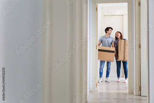 Young couple moving carton boxes in new empty apartment with opened door