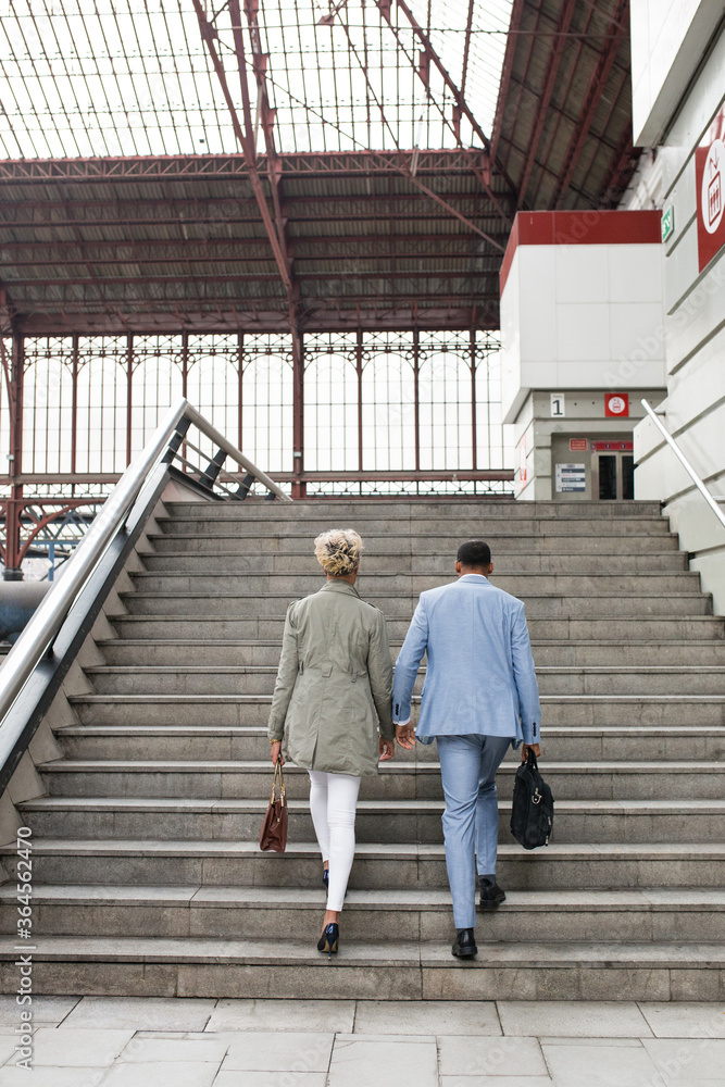 Elegant black woman and man having talk while walking down stairs on railway station. Elegant black woman and man having talk while walking down stairs on railway station.