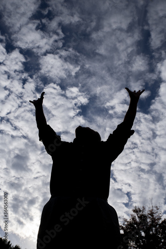 Male silhouette looking up at and reaching stretching praising challenging yelling pleading screaming at the blue and white cloud filled sky