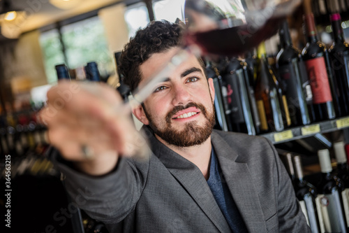 Handsome bearded man in elegant outfit exploring color of red wine in glass having time in wine house. photo