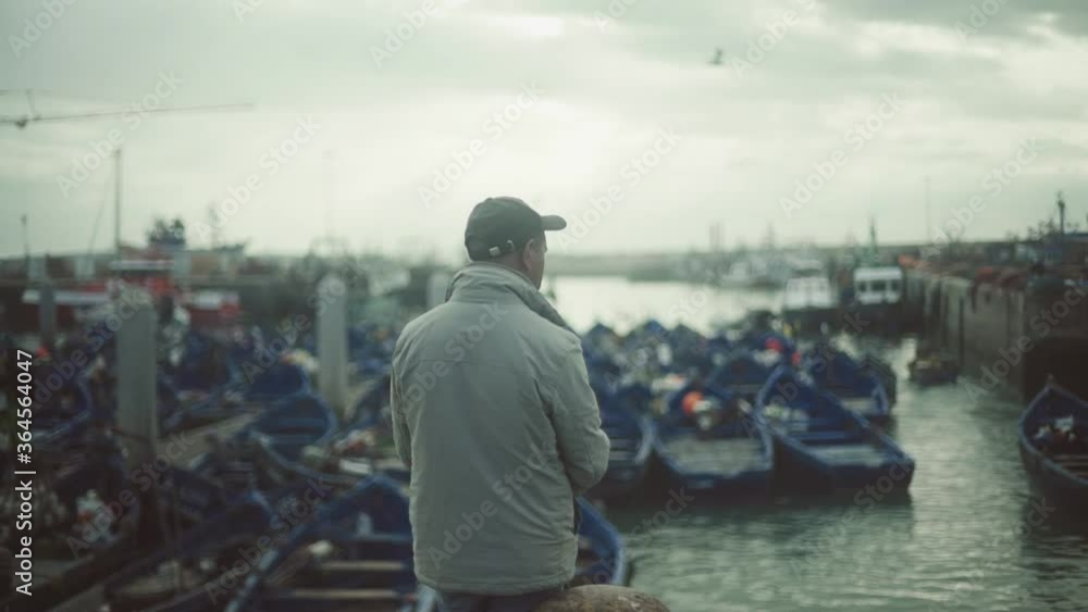 man standing and watching in front of harbor of Essaouira Morocco looking many blue fishing boats , authentic African sea life man standing and watching in front of harbor of Essaouira Morocco looking many blue fishing boats , authentic African sea life