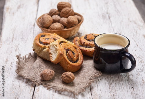 Basket of homemade buns with jam, served on old wooden table with walnuts and cup of milk