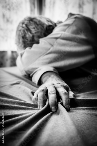 Troubled man person, hopeless, sadness, loss, depression, grief or crying sitting alone at table, clutching table cloth with face hidden and select focus on hand in B&W black & white monochrome