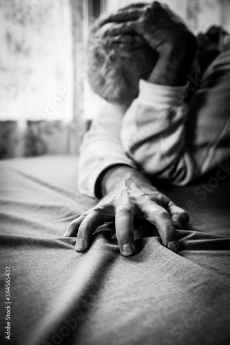 Troubled man person, sad, sadness, loss, depression, grief or crying sitting alone at table, clutching table cloth with face hidden and select focus on hand in B&W black & white monochrome