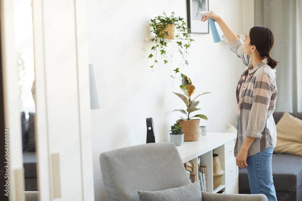 Young woman taking care about her flowers in the room she splashing water from the bottle on them Young woman taking care about her flowers in the room she splashing water from the bottle on them