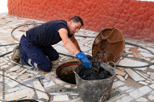 Obraz na płótnie Worker cleans the drains hatch and removes dirt and debris from the sewer on the street. Repair of sewage or underground utilities, cleans drains. Plumber cleans the sewer. w salonie