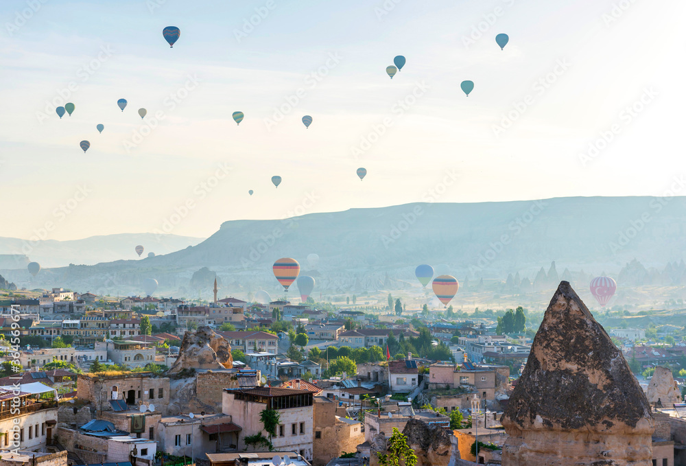 Hot air balloons flight - view of Goreme valley in Turkey. Panorama of Cappadocia - wide angel landscape with colorful hot balloons flying over mountain peaks of ancient cave town Uchisar.