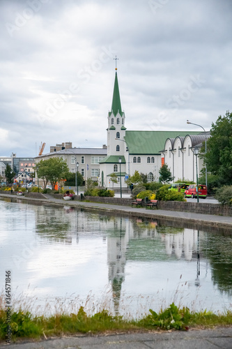REYKJAVIK, ICELAND - AUGUST 11, 2019: Lake Tjornin with church on a cloudy summer day © jovannig