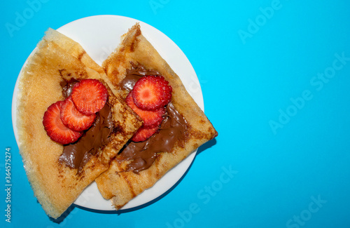 Fresh thin pancakes with chocolate paste and strawberry on blue background with copy space. Russian, English style pancakes for Pancake Week. 