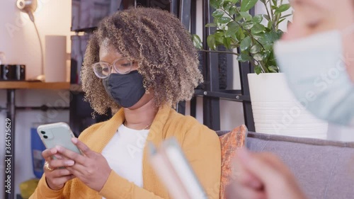 Two colleagues social distance on a couch at work while wearing masks and using their phones photo