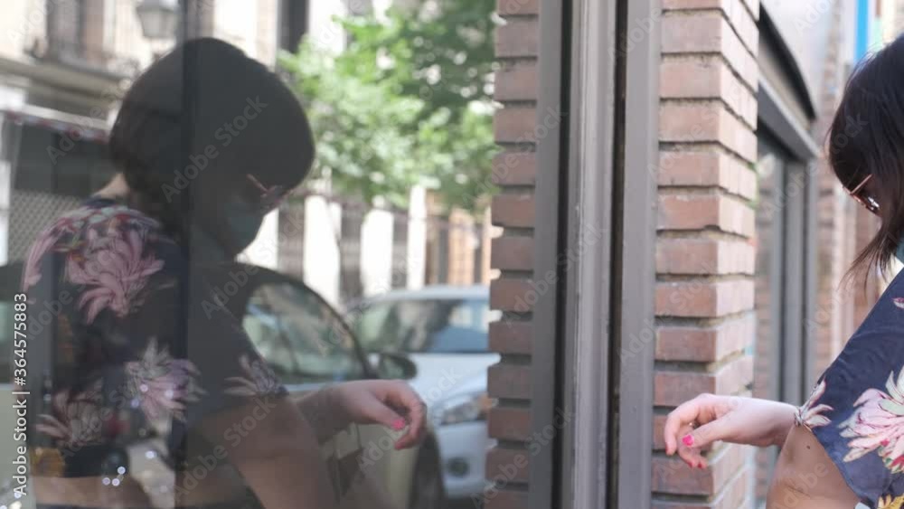 Young caucasian woman looking at a showcase and applying sanitizer gel on her hands before entering. Coronavirus prevention concept. Young caucasian woman looking at a showcase and applying sanitizer gel on her hands before entering. Coronavirus prevention concept.