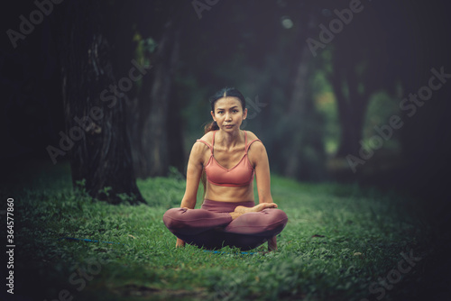 Asian model poses yoga in a park on a natural green background, health care concept, beautiful body structure, fit body