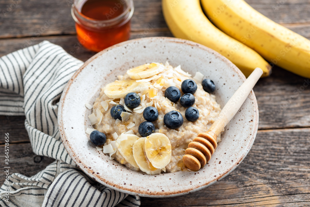 Oatmeal porridge with blueberries, bananas and honey in a bowl on wooden table. Healthy breakfast food concept