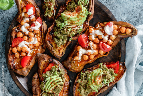 Baked sweet potato toast with roasted chickpeas, tomatoes, goat cheese, sauce guacamole, avocado, seedlings on wooden board over blue background. Healthy vegan food, clean eating, dieting, top view