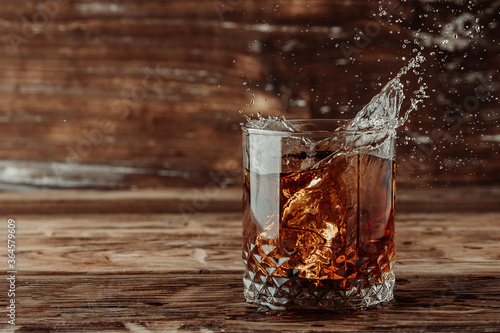 splashes in a whiskey glass on a wooden background.