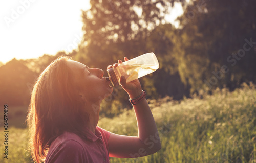 Girl drinking water with lemons from clear plastic bottle in contrast light during summer sunset