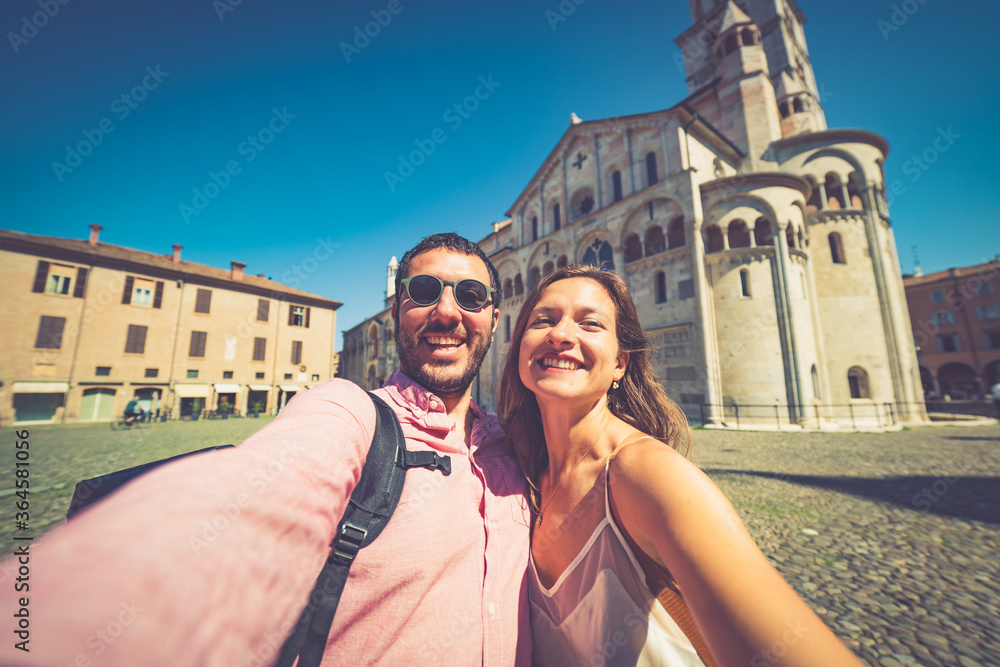 happy Tourist couple visit city center of Modena in the main square of the city taking selfie photo together. Major destination in Emilia-Romagna, Italy