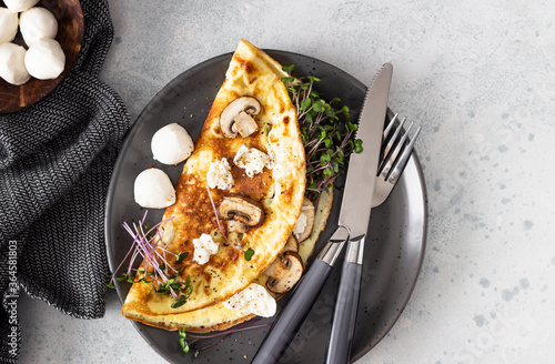 Bild auf Leinwand Homemade omelette with mushroom, mozzarella and microgreens on plate over light concrete background