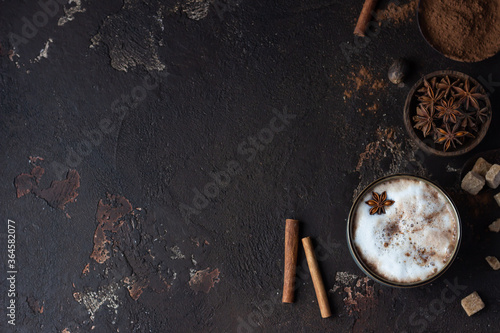 Homemade spicy hot chocolate with anise star, cinnamon sticks and bitter chocolate, dark brown concrete background. Top view. Copy space.