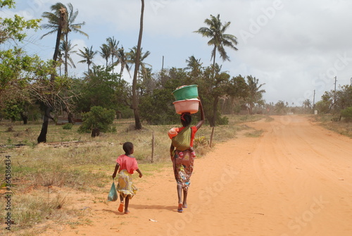 Kobieta z dzieckiem niosąca wodę szutrową drogą w Afryce w Mozambiku photo