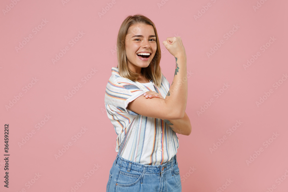 Cheerful young blonde woman girl in casual striped shirt posing isolated on pastel pink wall background studio portrait. People emotions lifestyle concept. Mock up copy space. Showing biceps, muscles. Cheerful young blonde woman girl in casual striped shirt posing isolated on pastel pink wall background studio portrait. People emotions lifestyle concept. Mock up copy space. Showing biceps, muscles.