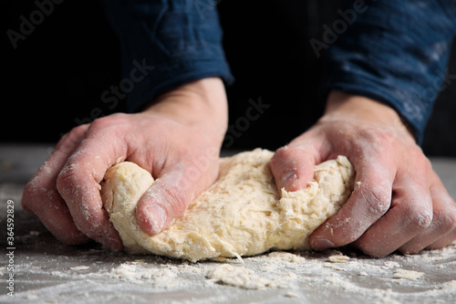 Thin male hands knead the dough for bread, pasta or pizza, close up. Closeup hand of chef baker kneading a dough