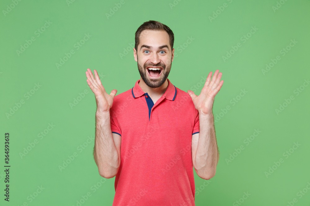 Surprised young bearded man guy in casual red pink t-shirt posing isolated on green wall background studio portrait. People lifestyle concept. Mock up copy space. Keeping mouth open, spreading hands. Surprised young bearded man guy in casual red pink t-shirt posing isolated on green wall background studio portrait. People lifestyle concept. Mock up copy space. Keeping mouth open, spreading hands.