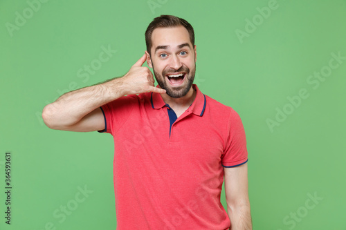 Excited young bearded man guy in casual red pink t-shirt posing isolated on green background studio portrait. People lifestyle concept. Mock up copy space. Doing phone gesture like says call me back.