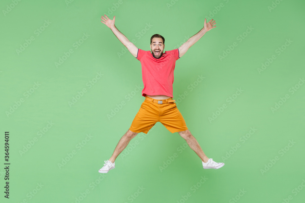 full length Excited young bearded man guy in casual red pink t-shirt posing isolated on green background studio portrait. People lifestyle concept. Mock up copy space. Jumping spreading hands and legs full length Excited young bearded man guy in casual red pink t-shirt posing isolated on green background studio portrait. People lifestyle concept. Mock up copy space. Jumping spreading hands and legs