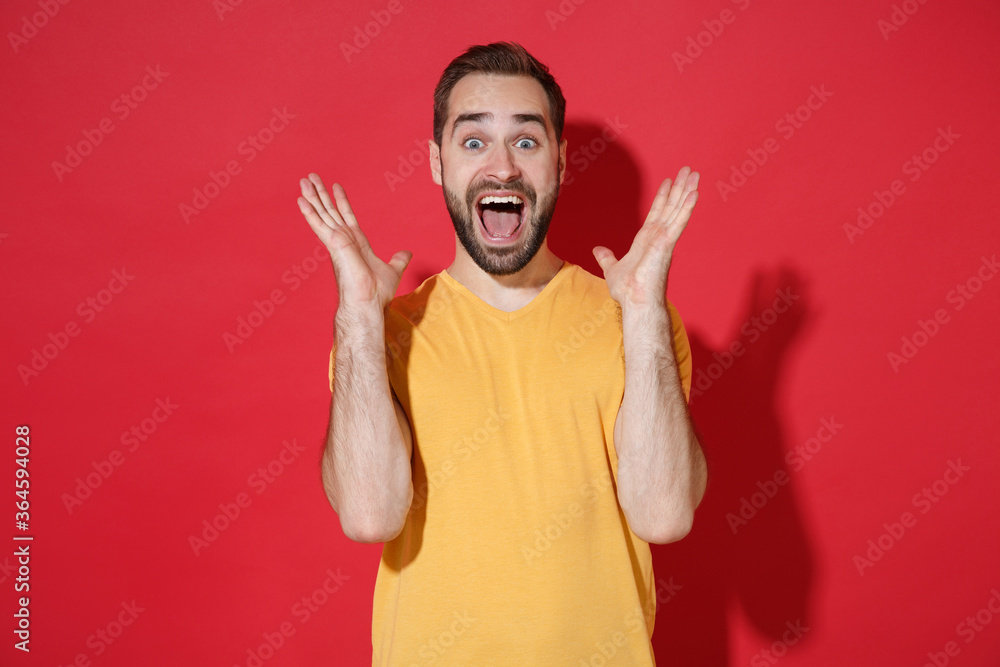 Surprised young bearded man guy in casual yellow t-shirt posing isolated on red background studio portrait. People emotions lifestyle concept. Mock up copy space. Keeping mouth open, spreading hands. Surprised young bearded man guy in casual yellow t-shirt posing isolated on red background studio portrait. People emotions lifestyle concept. Mock up copy space. Keeping mouth open, spreading hands.