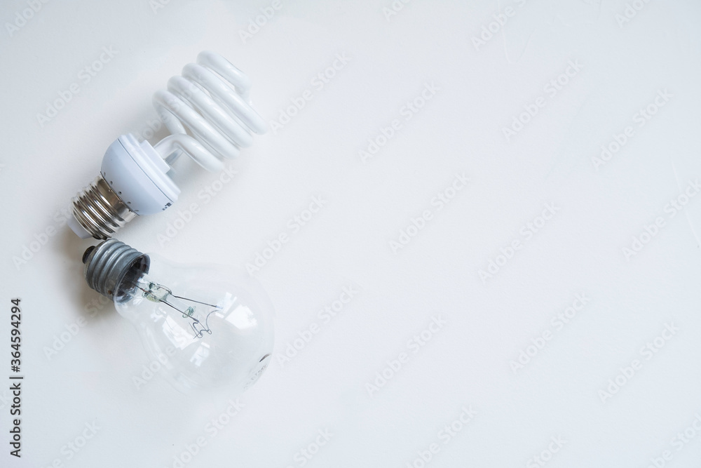 Two light bulbs one incandescent and one energy-saving lie on a light background. Past and Present (Future) Two light bulbs one incandescent and one energy-saving lie on a light background. Past and Present (Future)