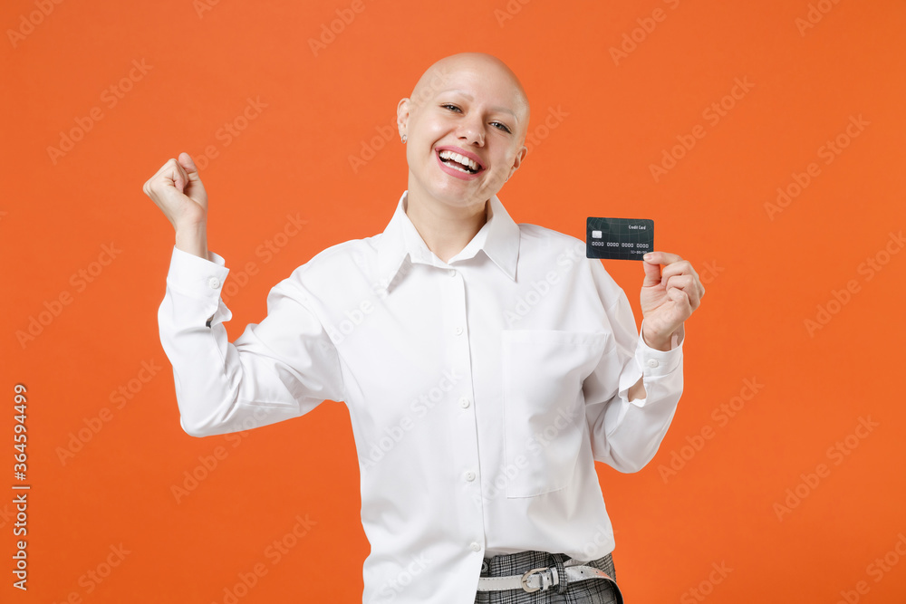 Happy young bald business woman girl in white shirt posing isolated on orange background. Achievement career wealth business concept. Mock up copy space. Hold credit bank card doing winner gesture. Happy young bald business woman girl in white shirt posing isolated on orange background. Achievement career wealth business concept. Mock up copy space. Hold credit bank card doing winner gesture.