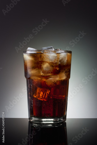 Tall glass with a cold dark drink, filled with pieces of ice,