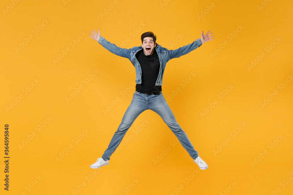 full length Shocked young man guy in casual denim clothes posing isolated on yellow background studio portrait. People sincere emotions lifestyle concept. Mock up copy space. Jump spreading hands legs
