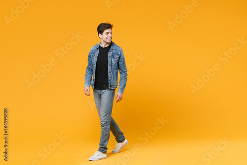 full length Smiling young man guy 20s in casual denim clothes posing isolated on yellow wall background studio portrait. People sincere emotions lifestyle concept. Mock up copy space. Looking aside.
