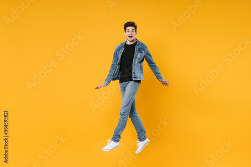 full length Excited young man guy in casual denim clothes posing isolated on yellow background studio portrait. People sincere emotions lifestyle concept. Mock up copy space. Jump spreading hands legs