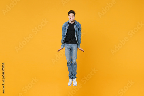 full length Smiling young man guy 20s in casual denim clothes posing isolated on yellow wall background studio portrait. People sincere emotions lifestyle concept. Mock up copy space. Jump having fun