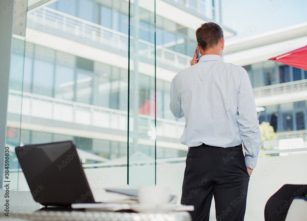 Fototapeta premium Businessman talking on cell phone at office window