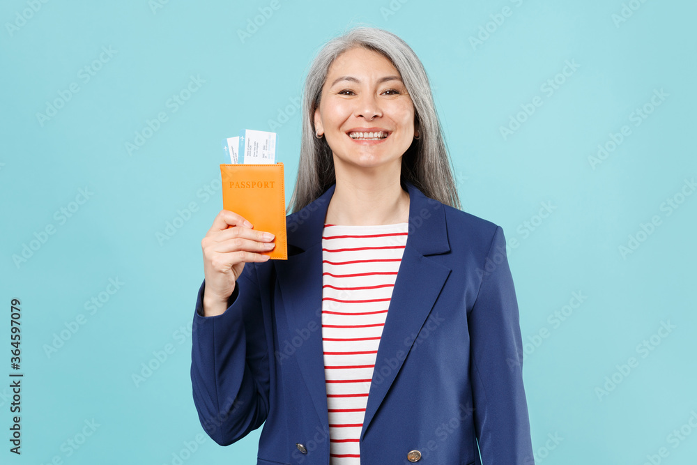 Smiling gray-haired business woman in blue suit posing isolated on blue background studio portrait. Achievement career wealth business concept. Mock up copy space. Hold passport tickets boarding pass. Smiling gray-haired business woman in blue suit posing isolated on blue background studio portrait. Achievement career wealth business concept. Mock up copy space. Hold passport tickets boarding pass.