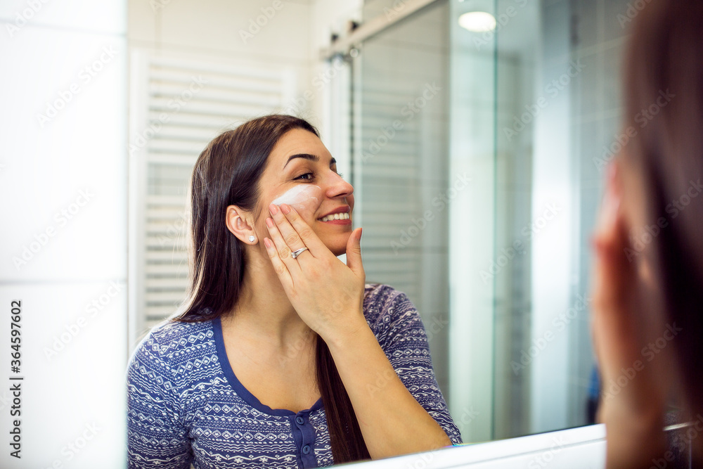 Portrait of lady applying cream on face while looking at reflection in bathroom Portrait of lady applying cream on face while looking at reflection in bathroom
