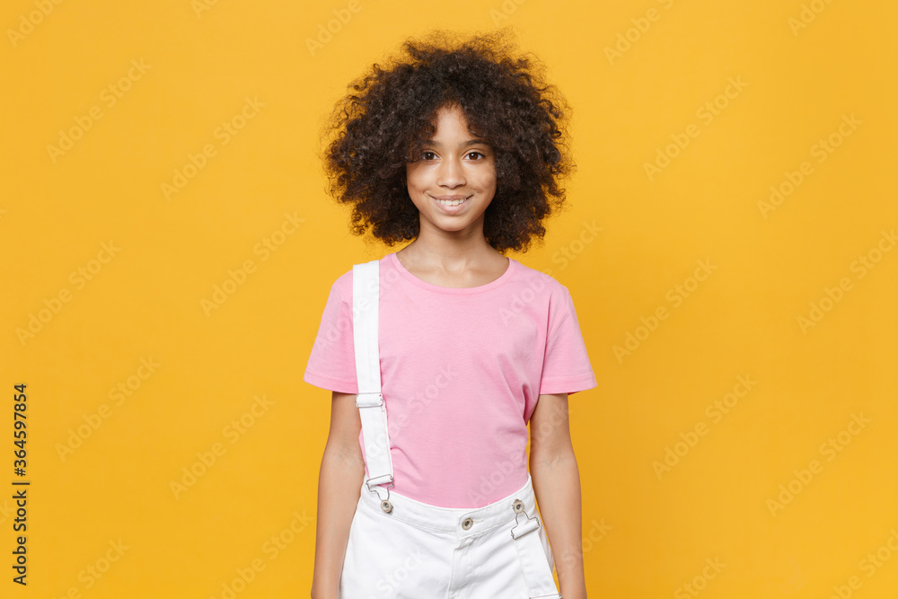 Smiling little african american kid girl 12-13 years old in casual pink t-shirt isolated on yellow background children studio portrait. Childhood lifestyle concept. Mock up copy space. Looking camera. Smiling little african american kid girl 12-13 years old in casual pink t-shirt isolated on yellow background children studio portrait. Childhood lifestyle concept. Mock up copy space. Looking camera.
