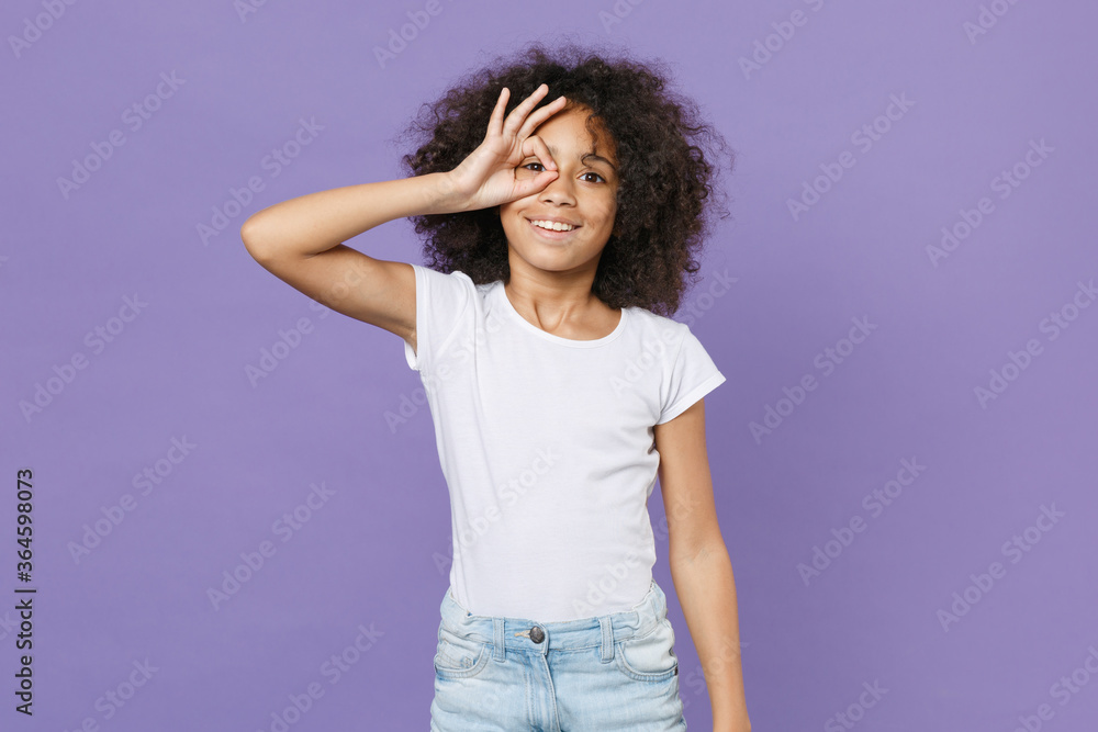 Funny little african american kid girl 12-13 years old in white t-shirt isolated on violet background studio. Childhood lifestyle concept. Holding hands near eyes, imitating glasses or binoculars. Funny little african american kid girl 12-13 years old in white t-shirt isolated on violet background studio. Childhood lifestyle concept. Holding hands near eyes, imitating glasses or binoculars.