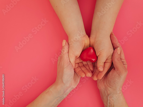 Fototapeta Naklejka Na Ścianę i Meble -  hands of mom and baby hold a heart on a colored background